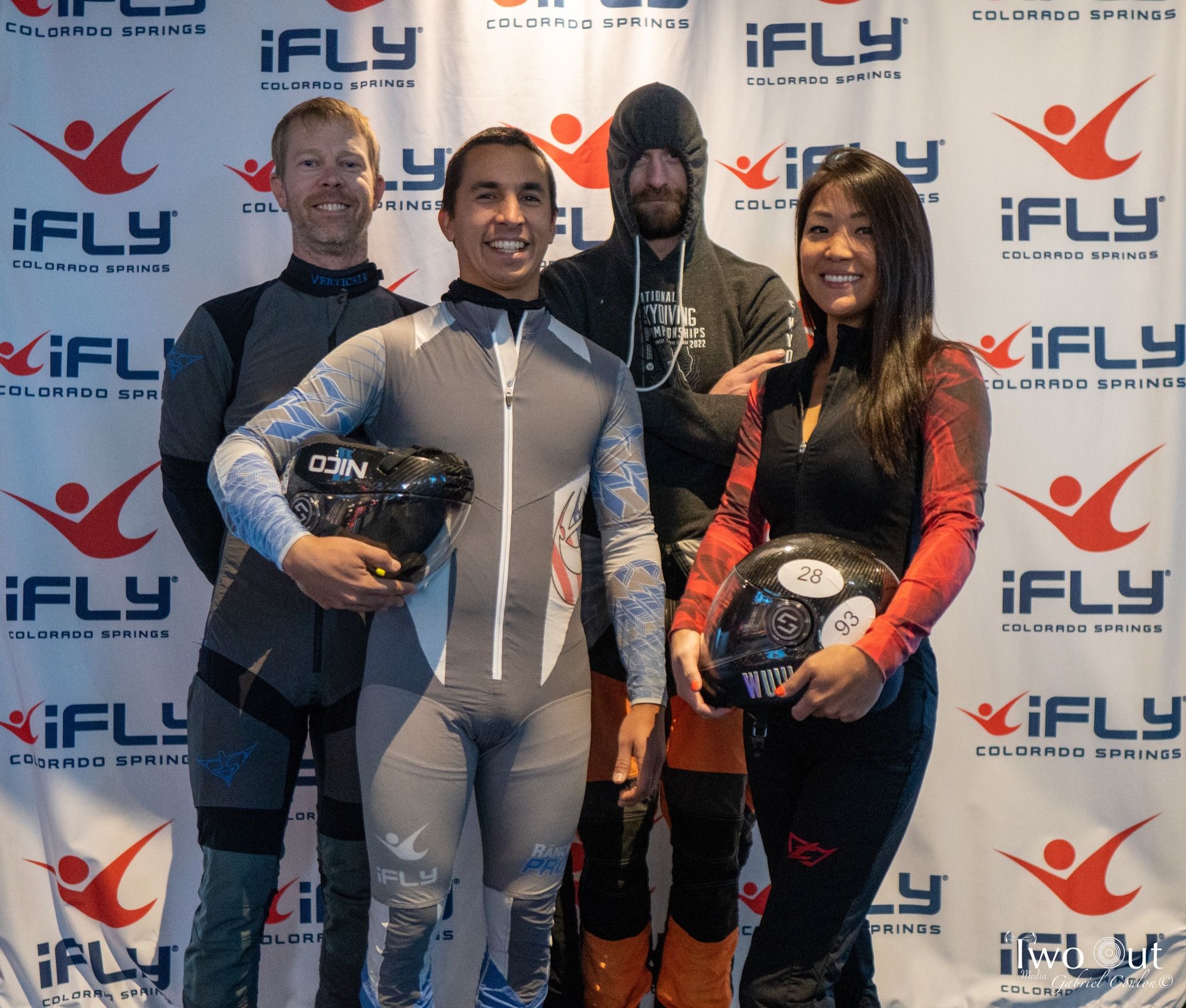 Four competitors in flight suits posing with their helmets at the step-and-repeat