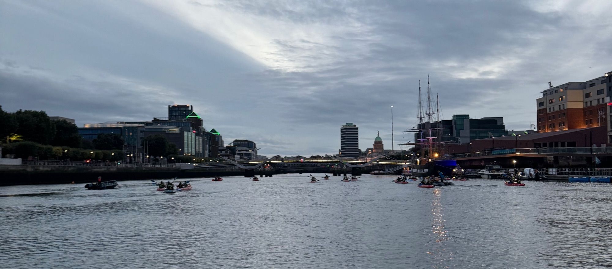 The kayak group spread across the river at dusk with the city lit up behind