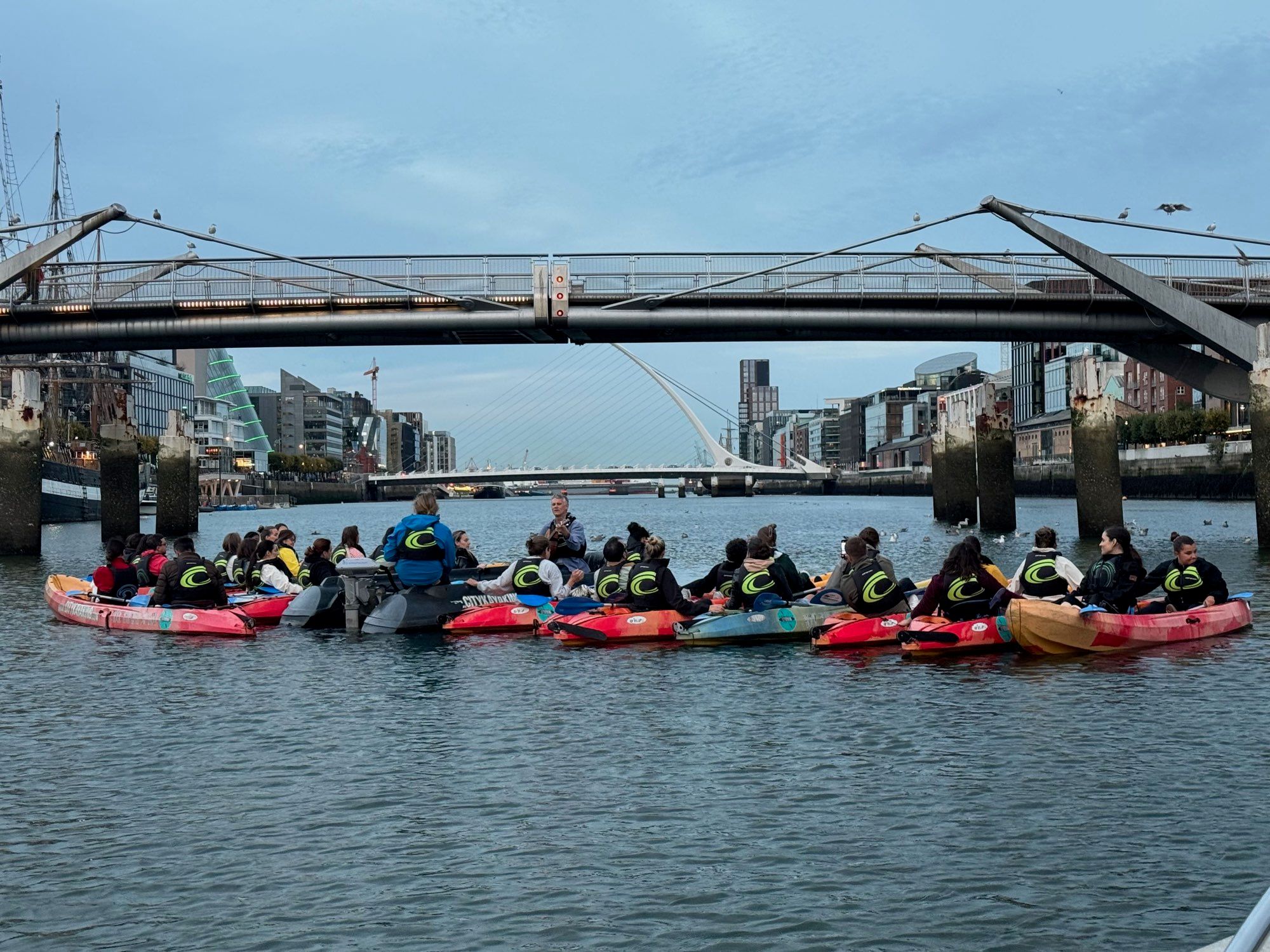 The kayak group rafted together under a footbridge with Dublin's docklands behind