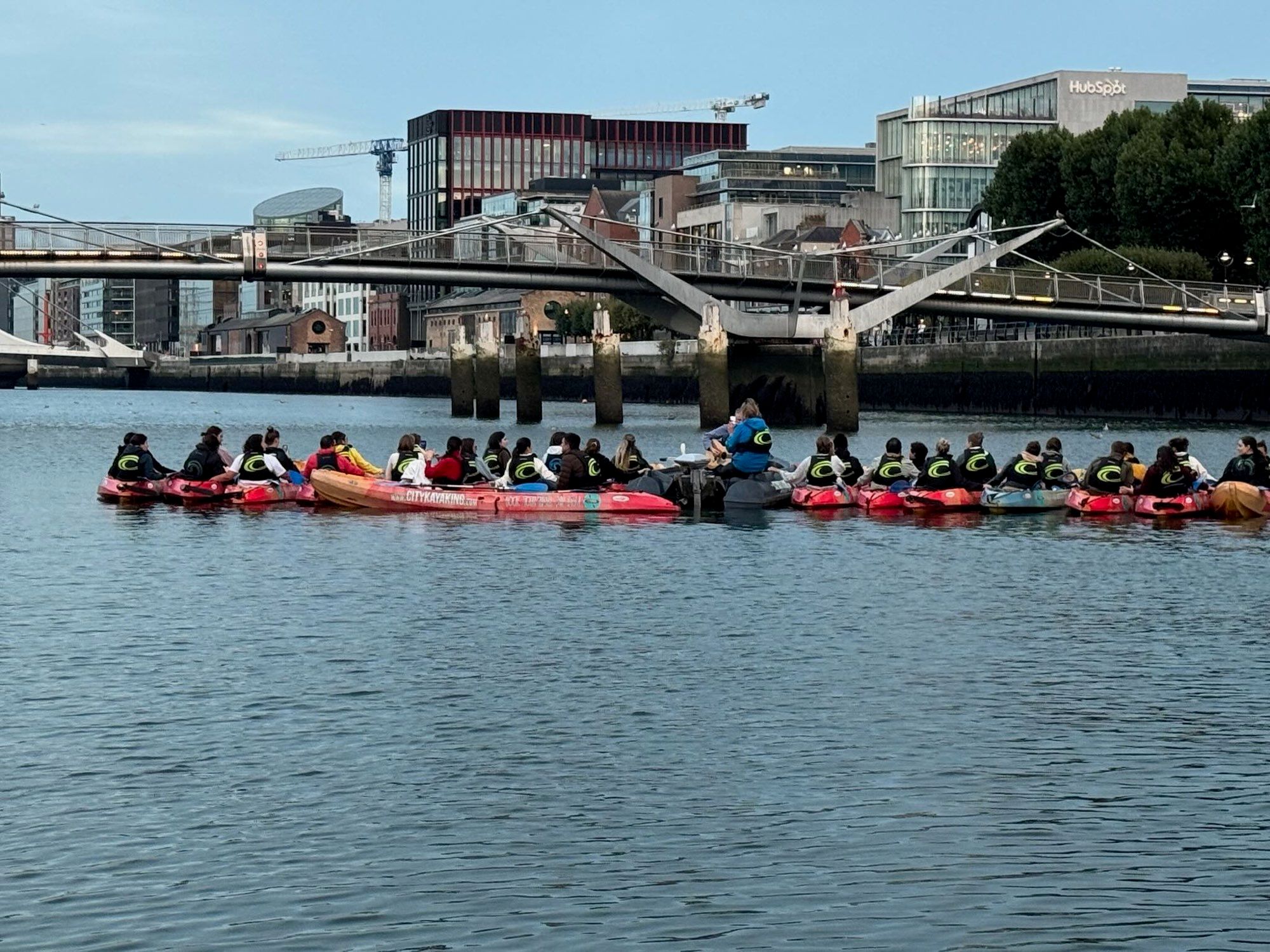 Wide shot of the kayak group gathered on the river at dusk with the city skyline behind
