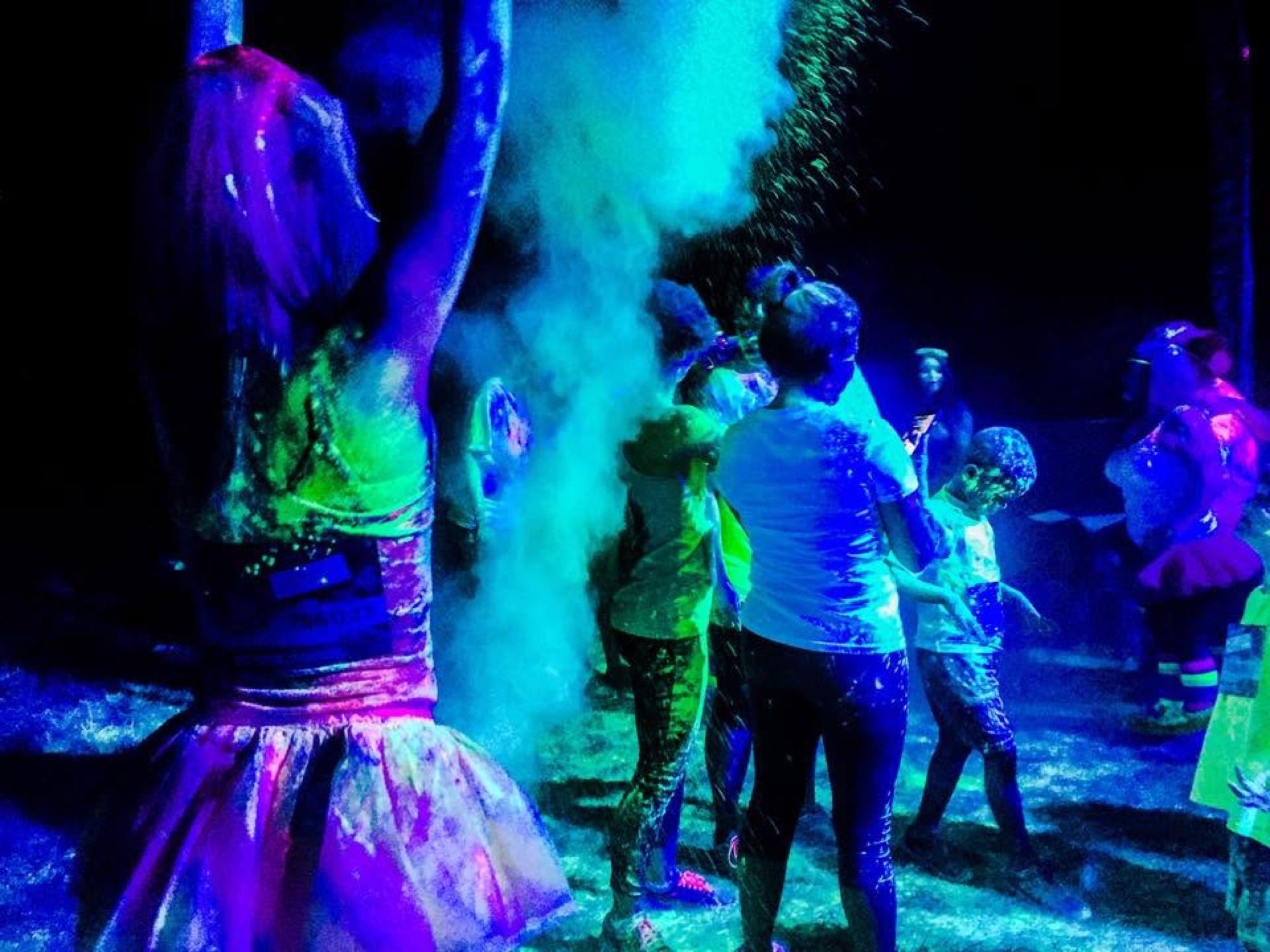 Runners in glowing UV body paint dancing at a nighttime colour run