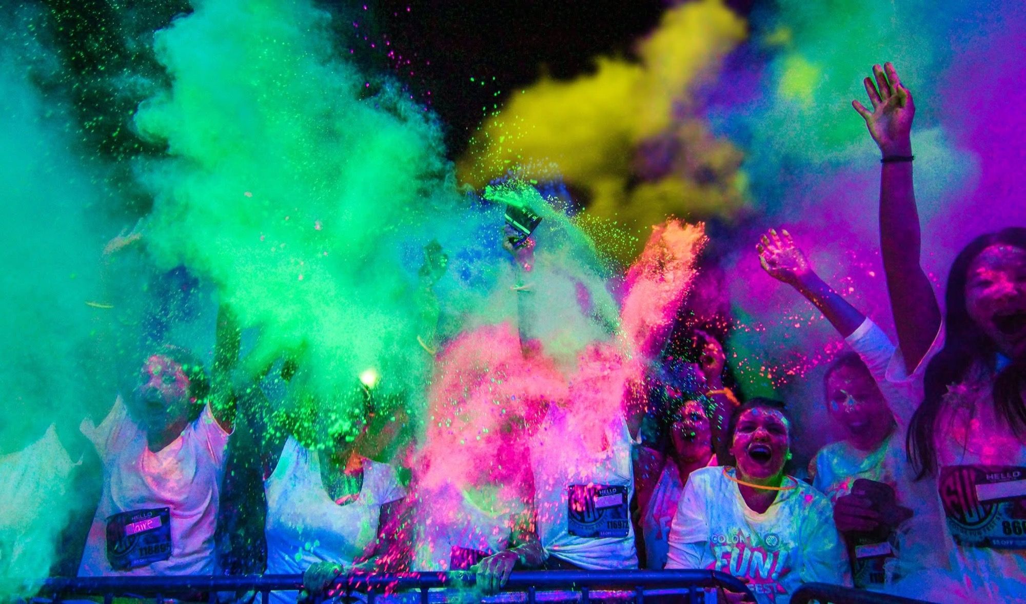 Crowd raising glowing hands amid coloured powder at a blacklight colour run