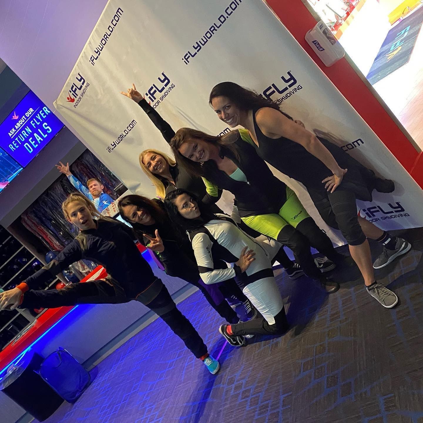 Group of women posing playfully in front of an iFly step-and-repeat banner