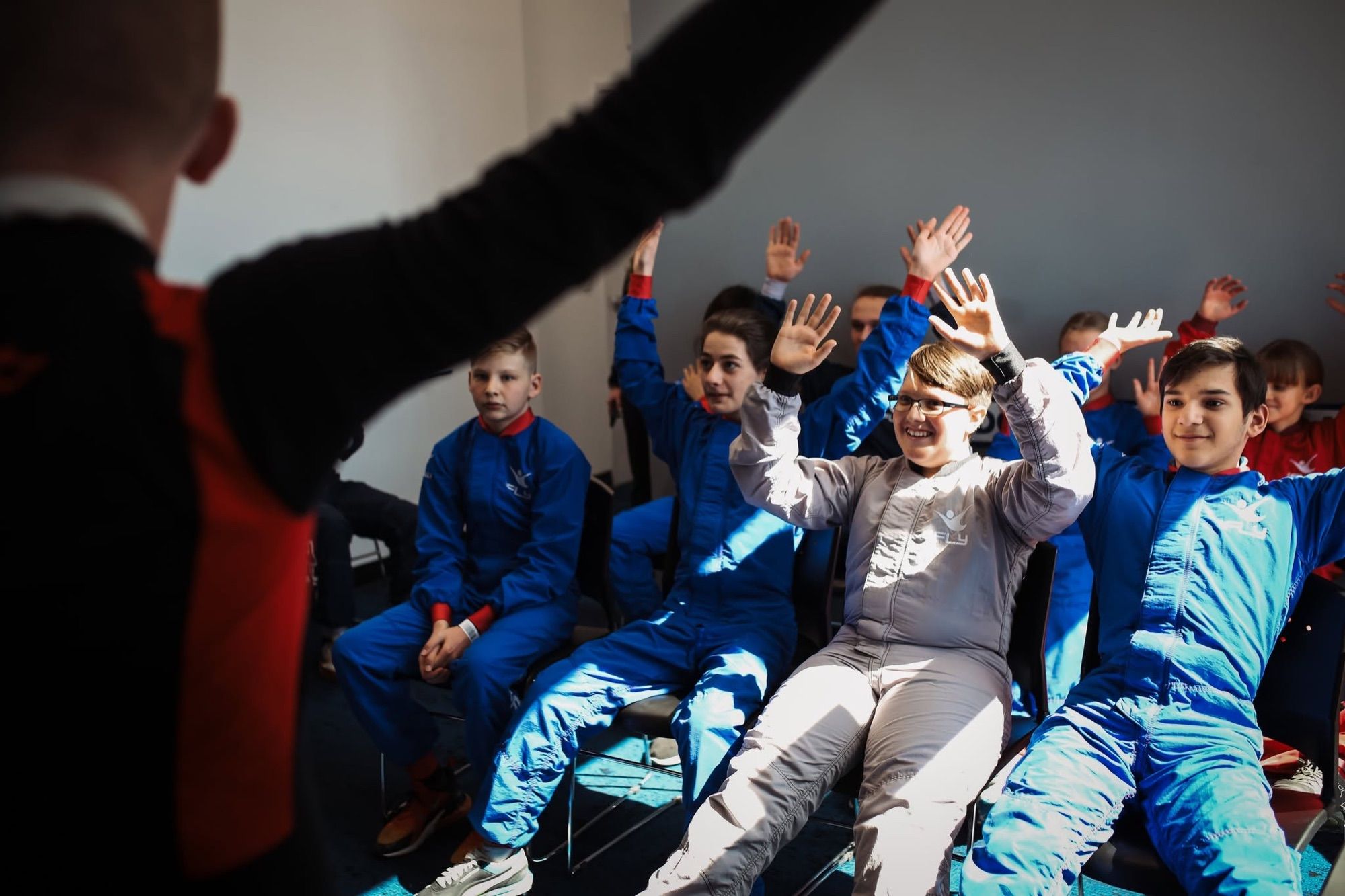 Kids in flight suits raising their hands during a STEM day briefing at iFly